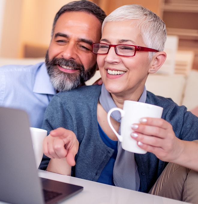 Smiling couple drinking coffee while looking at a computer